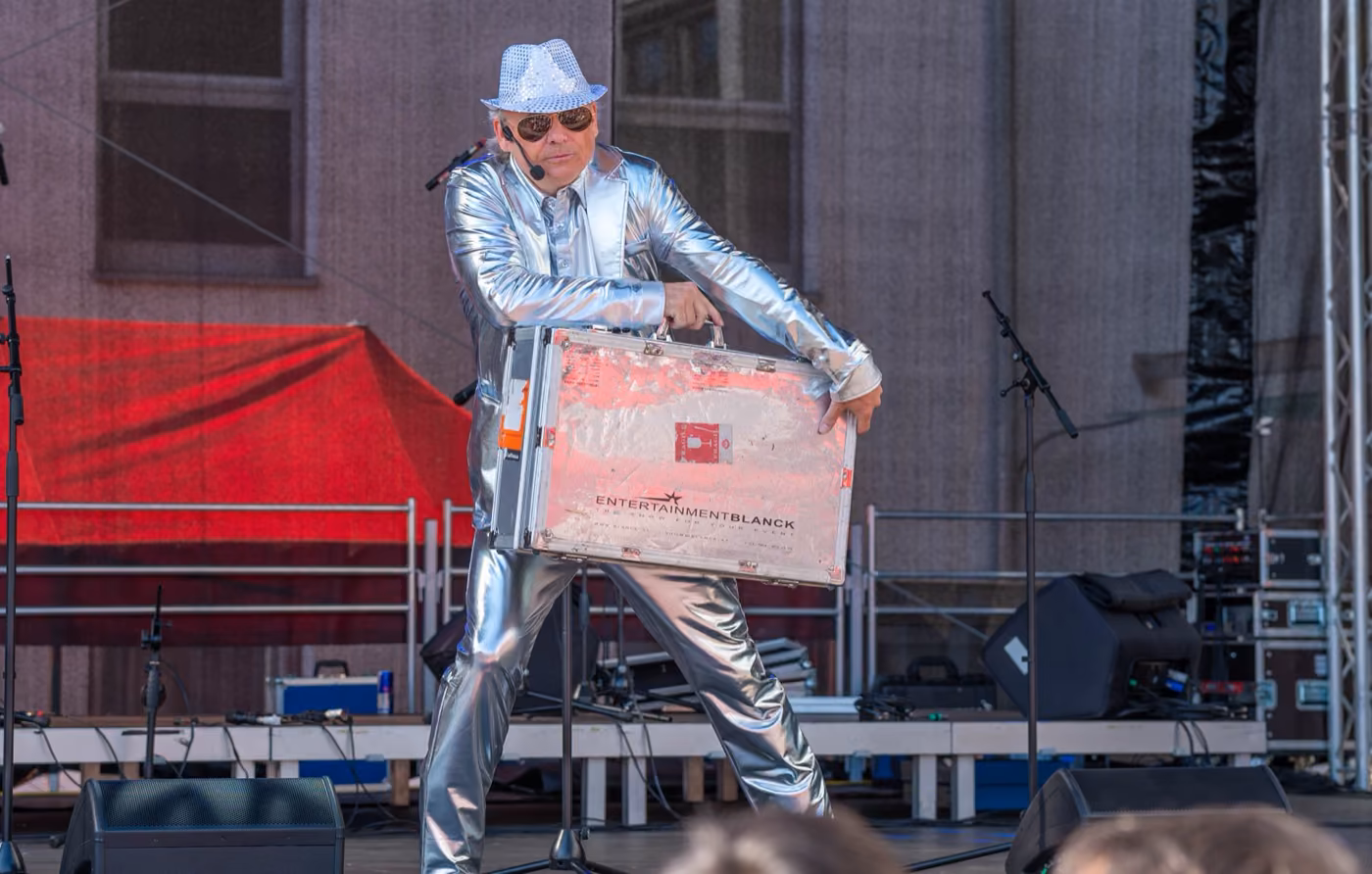 Axel Blanck im Silberanzug auf der Bühne mit Showkoffer